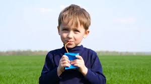 Young boy is drinking a juice box drink outside.