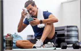 Man is sitting on the floor post workout. Smiling as he wipes his forehead with a towel.