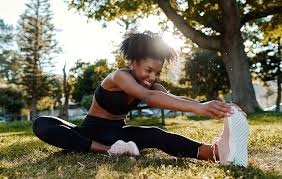 Girl stretching outside before a workout on the grass under trees.